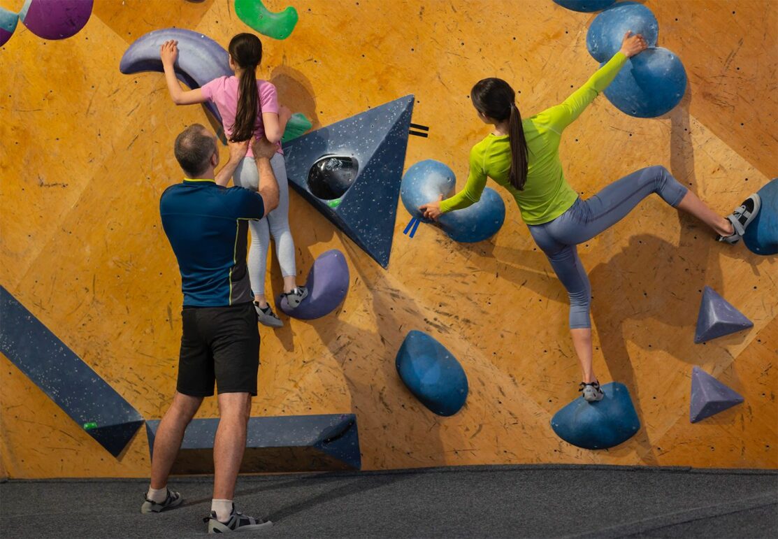 Familia formada por padre, madre e hija practicando escalada indoor en un centro Climbat, ideal para iniciarse en la escalada en familia en un entorno seguro y adaptado.