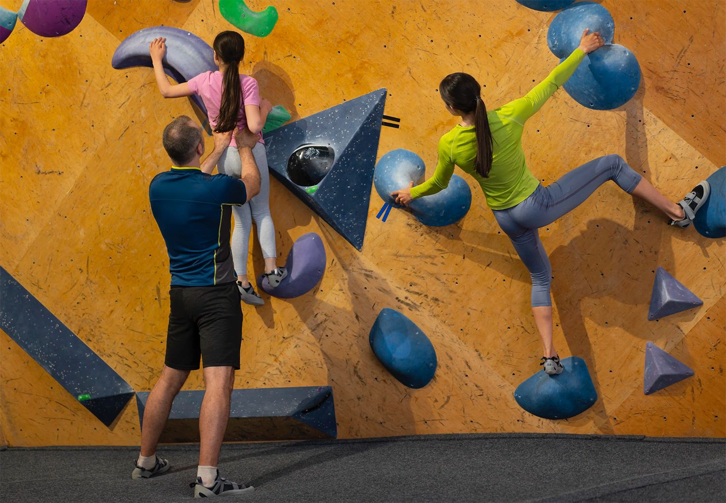 Familia formada por padre, madre e hija practicando escalada indoor en un centro Climbat, ideal para iniciarse en la escalada en familia en un entorno seguro y adaptado.