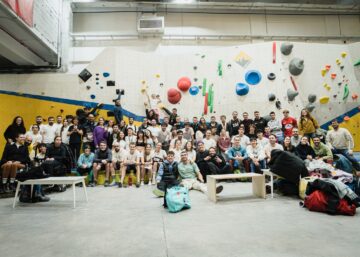 Grupo numeroso de participantes posando en un rocódromo durante un evento de escalada en bloque.