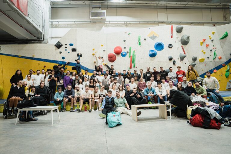 Grupo numeroso de participantes posando en un rocódromo durante un evento de escalada en bloque.